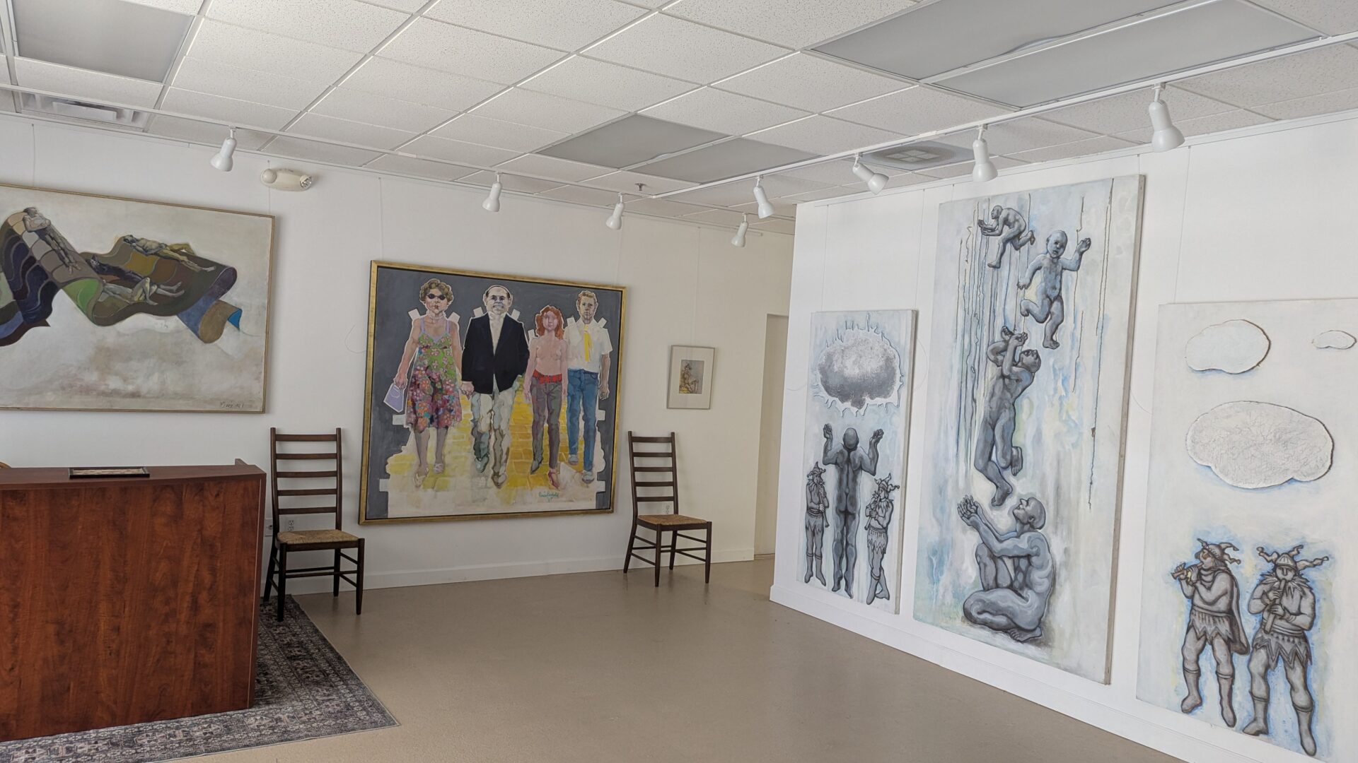 Art gallery room with paintings and two chairs.